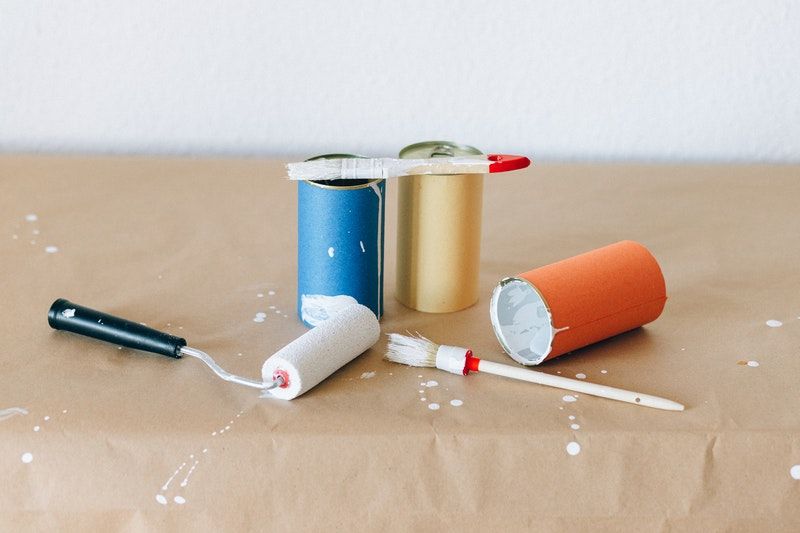 A roller and two paintbrushes with three mini cans of paint