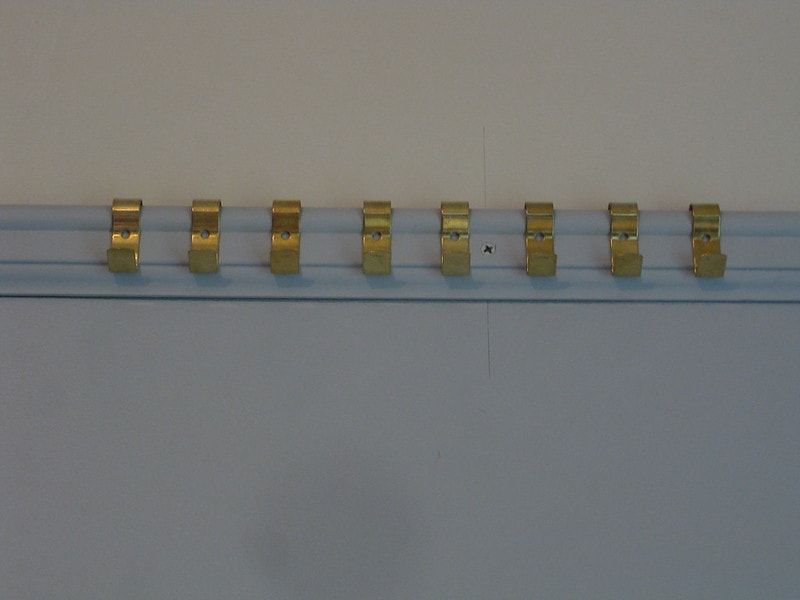 A closeup of a picture rail with gold hooks along it