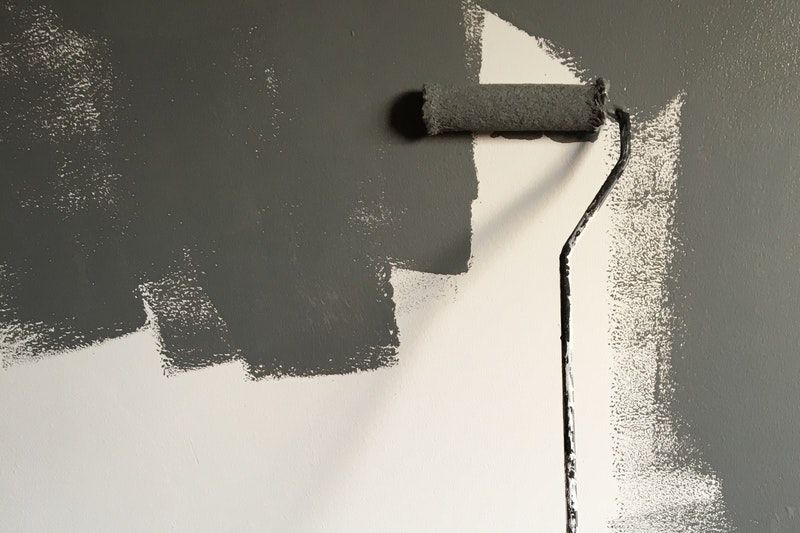 A roller being used to coat white wall in grey paint