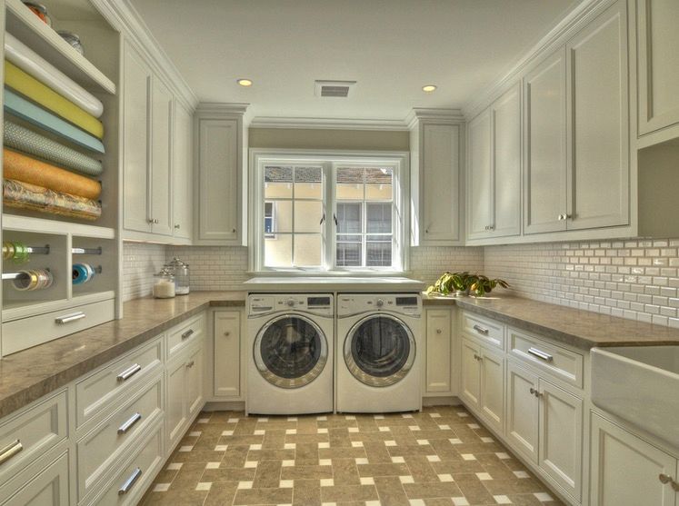 Modern laundry room with upper and lower cabinetry on either side with a washer and dryer below a large paned window