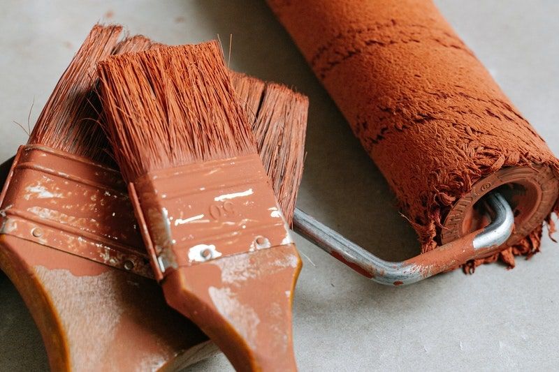 A closeup of paintbrushes and a roller covered in orange paint