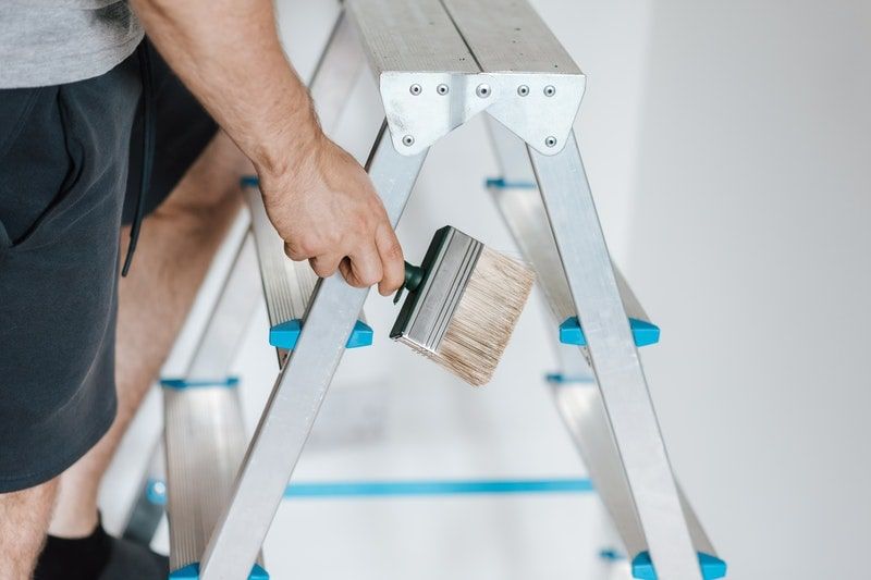 A closeup of a man on a step ladder, holding a paintbrush