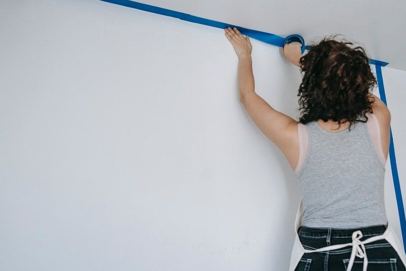 A woman applying blue painter’s tape along the edge of a ceiling