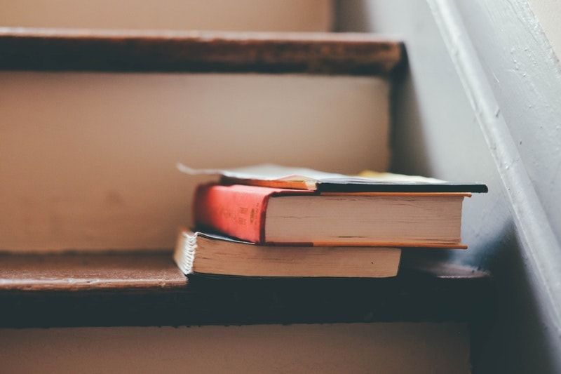 A closeup of two books on a wooden staircase with beige risers