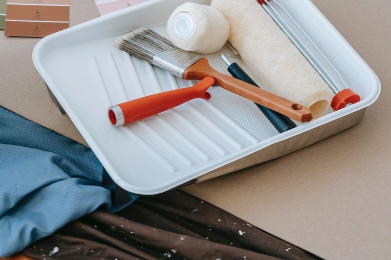 A paintbrush and rollers places in a paint tray