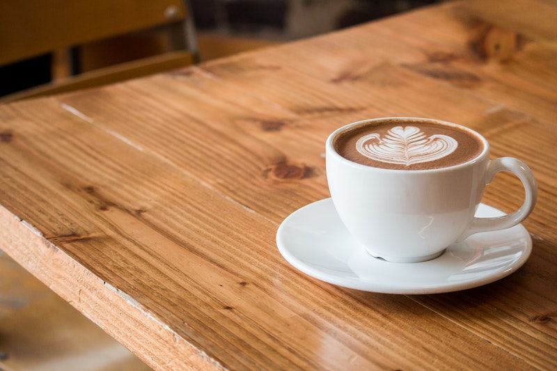 A closeup of a latte sitting on a polyurethane-coated wooden table