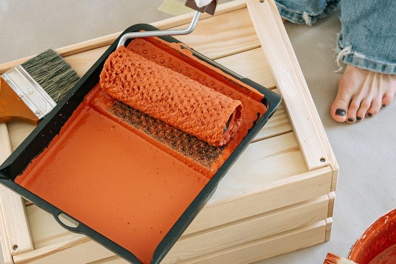 An orange paint covered roller sitting in a paint tray