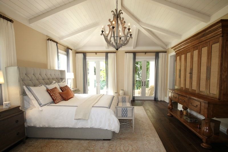 A large bedroom with an intricate ceiling, a beautiful chandelier, large windows, and a patio door