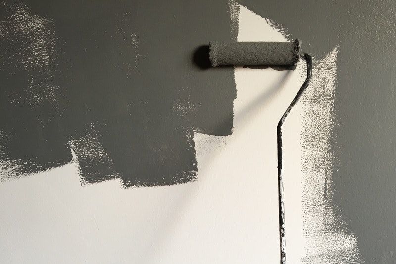 A roller painting dark grey paint on a white wall