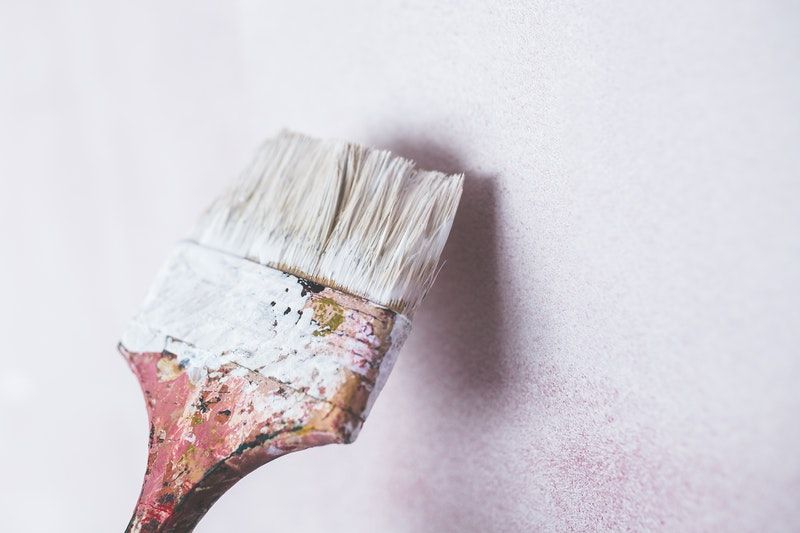A flat paintbrush applying white paint to a white wall