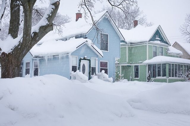 A blue two-storey house and front yard covered in snow, with a neighbouring green two-story home on the right