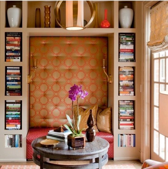 Inset reading nook with shelves above, built-in shelving on either side, a red bench, and padded metallic gold and red back wall