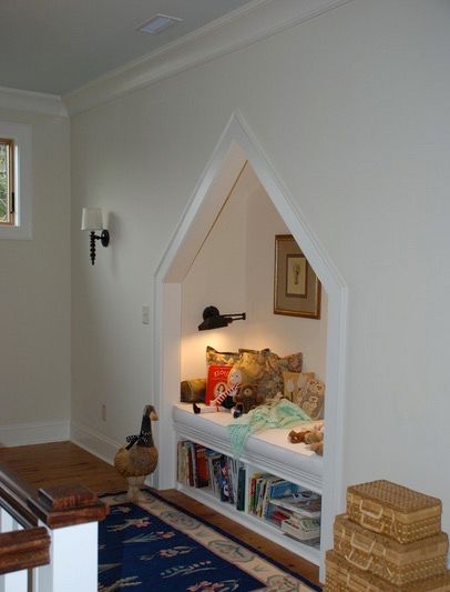 Children's reading nook (with bench, pillows, and overhead light) inset into the wall with a peak, along with shelving at the bottom for easy access to books