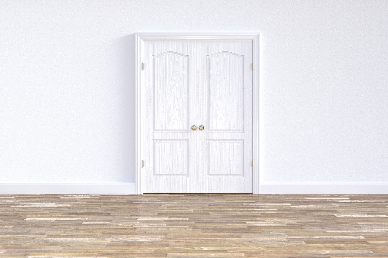 A white, wooden raised panel door in a bright, white room