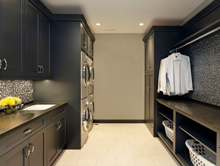 A large walk-in closet with dark espresso upper and lower storage cabinets leading to two sets of stacked stainless washers and dryers, and open lower shelves with a closet rod on the right