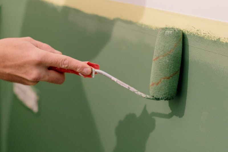 A closeup of a paint roller being used to apply green paint to part of a wall