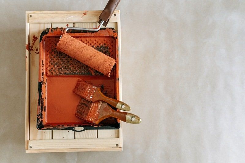 A photo of a roller and brushes inside a paint tray filled with orange paint
