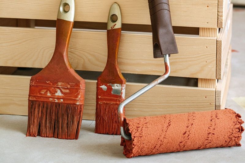 A closeup of two brushes and a roller covered in orange paint