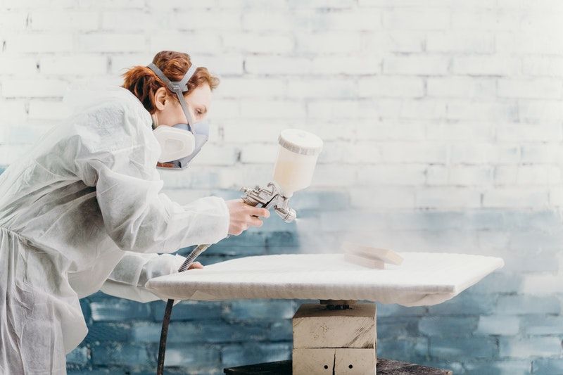 A painter in protective gear using a spray gun to paint pieces of wood white