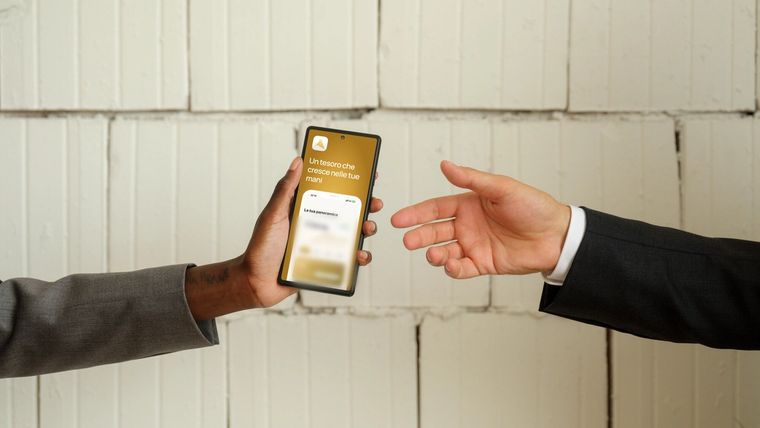 Due mani si passano uno smartphone con l'app Aurelia Gold aperta sulla schermata di benvenuto