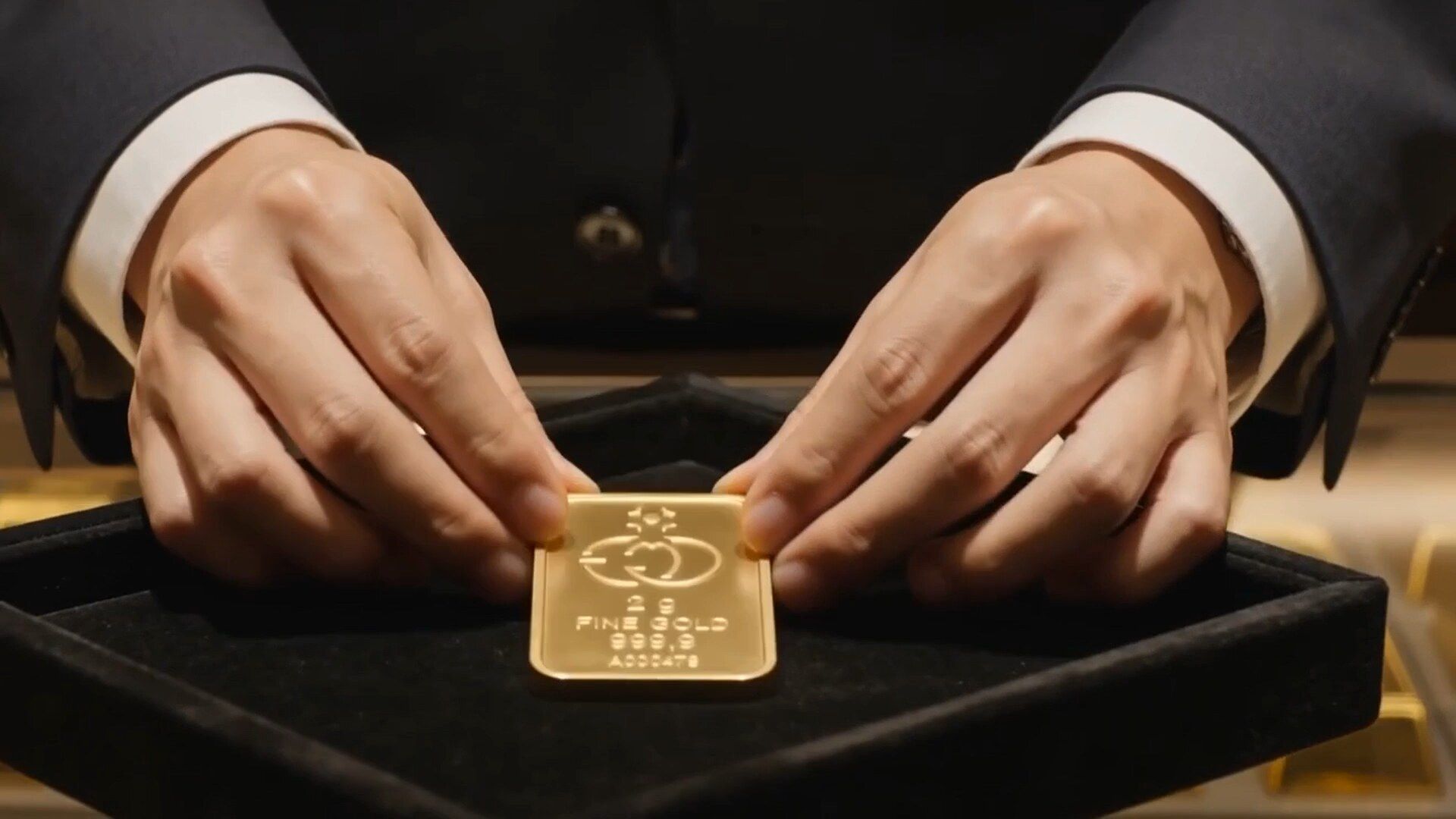 Le mani di un operatore posano un lingotto d'oro da 2 grammi su un vassoio di velluto nero
