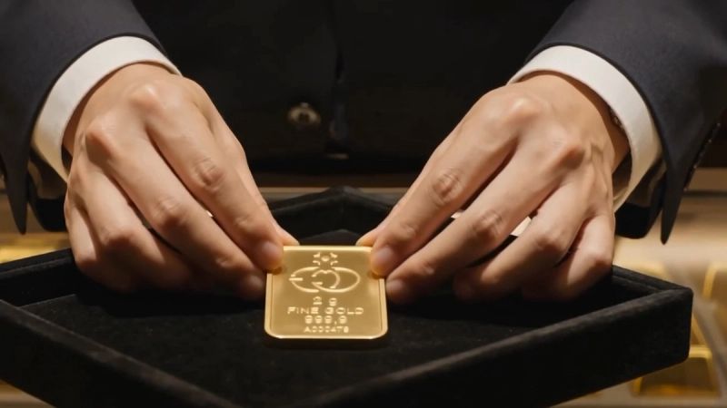 Le mani di un operatore posano un lingotto d'oro da 2 grammi su un vassoio di velluto nero