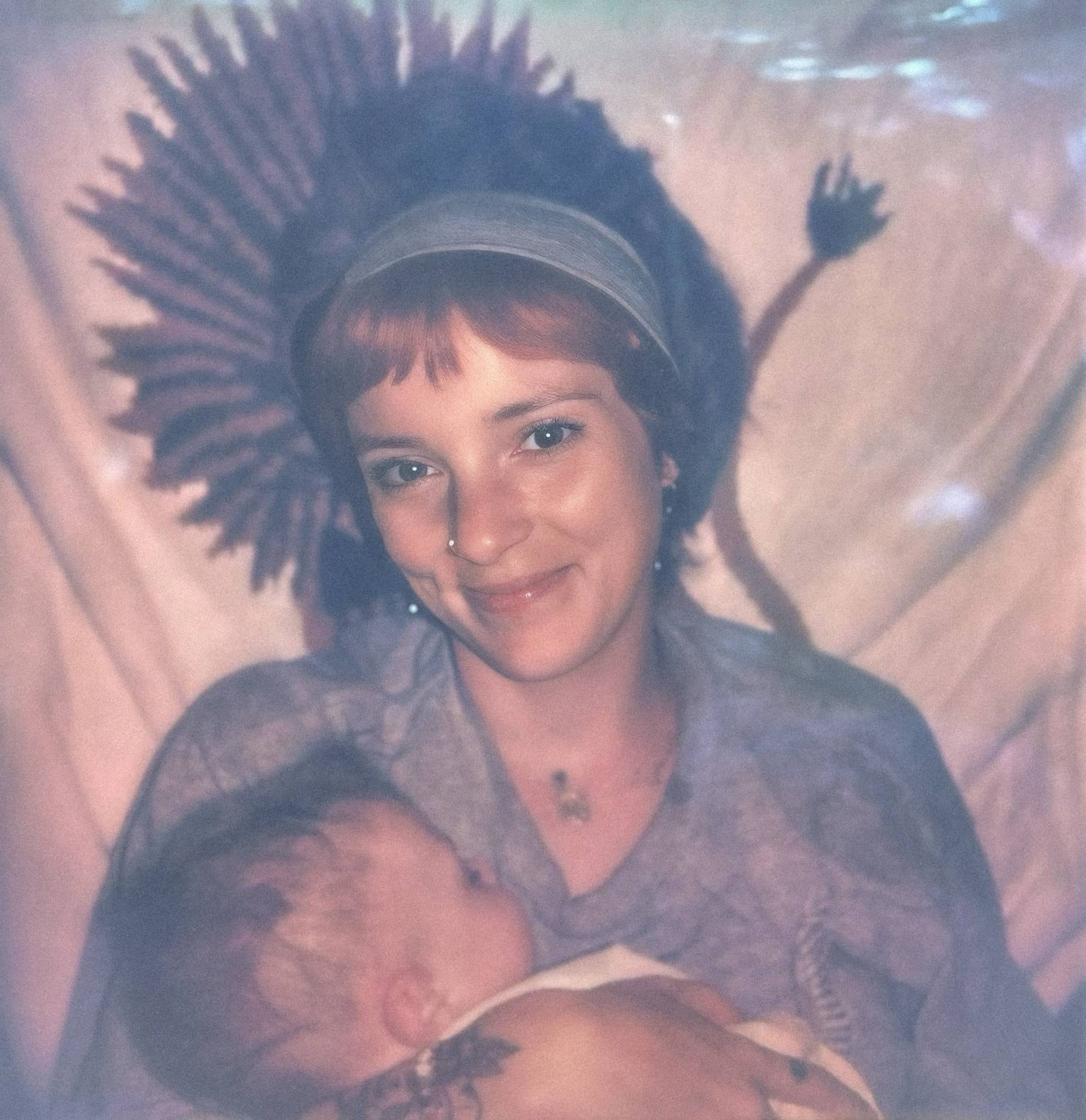 Birdie smiling, holding a sleeping newborn against her chest