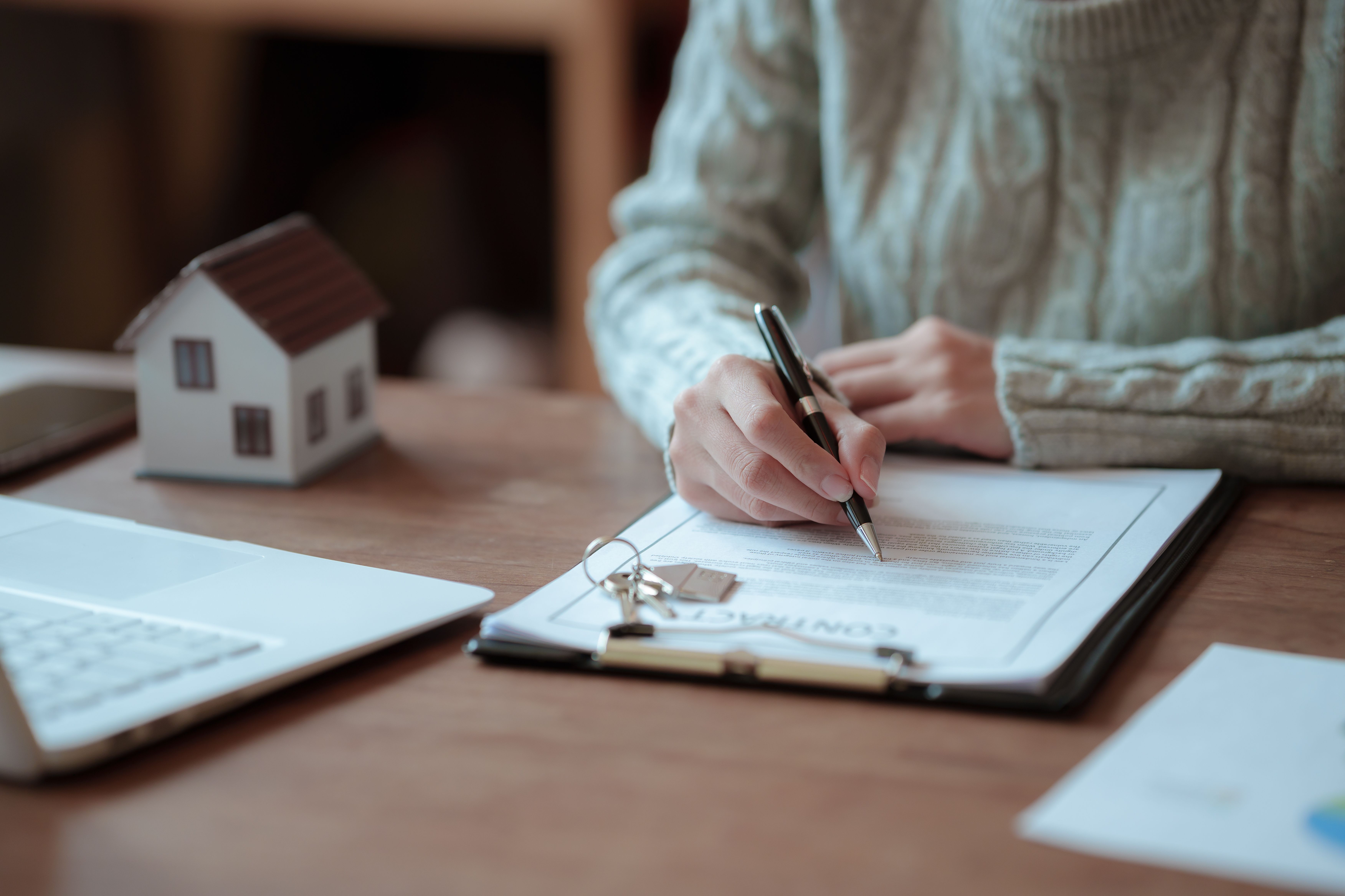 Tenant signing a rental tenancy agreement beside house keys and a model home, representing periodic tenancies and tenant notice periods in England.