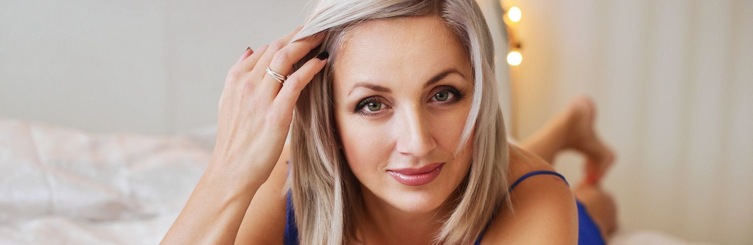 Woman engaging in a chat, representing 35p chat services in the UK, lying on her bed in a well lit room.