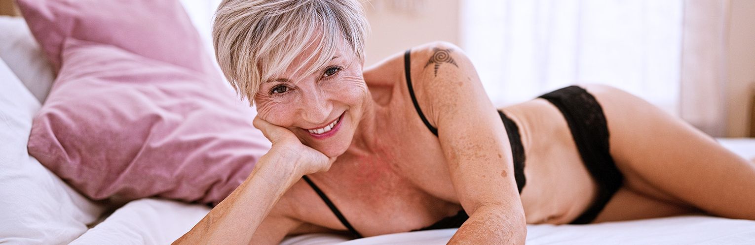 An older woman, 50+ - lying on her bed, in black lingerie