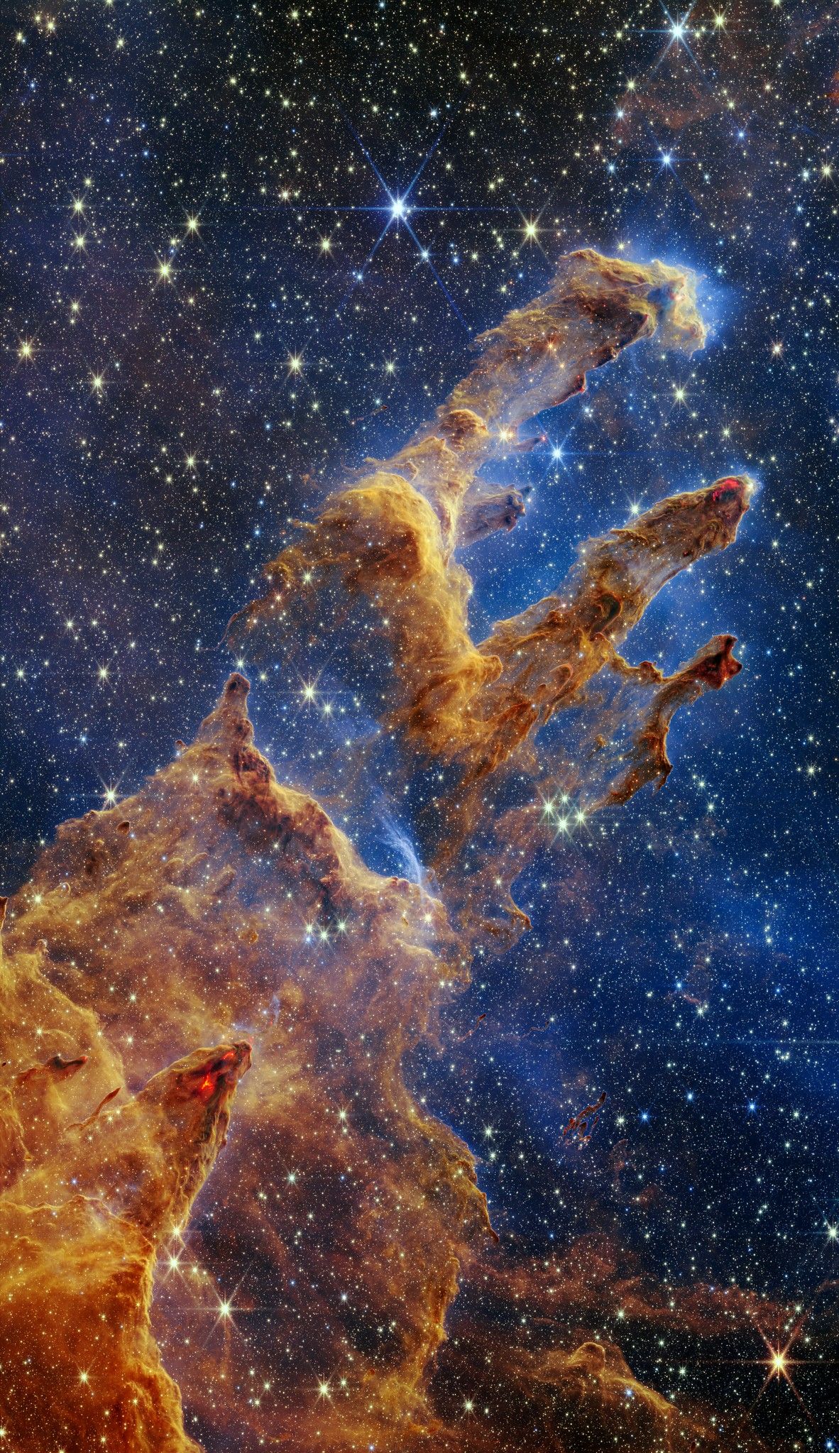 De "pillars of creation", een mosterdkleurige nevel tegen een donkerblauwe achtergrond. De nevel heeft twee opvallende en één iets minder opvallende 'pilaren' van gas en stof.
