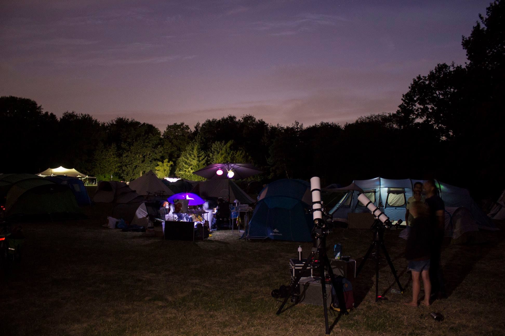 Foto van twee telescopen in het donker op een camping, omringd door tenten