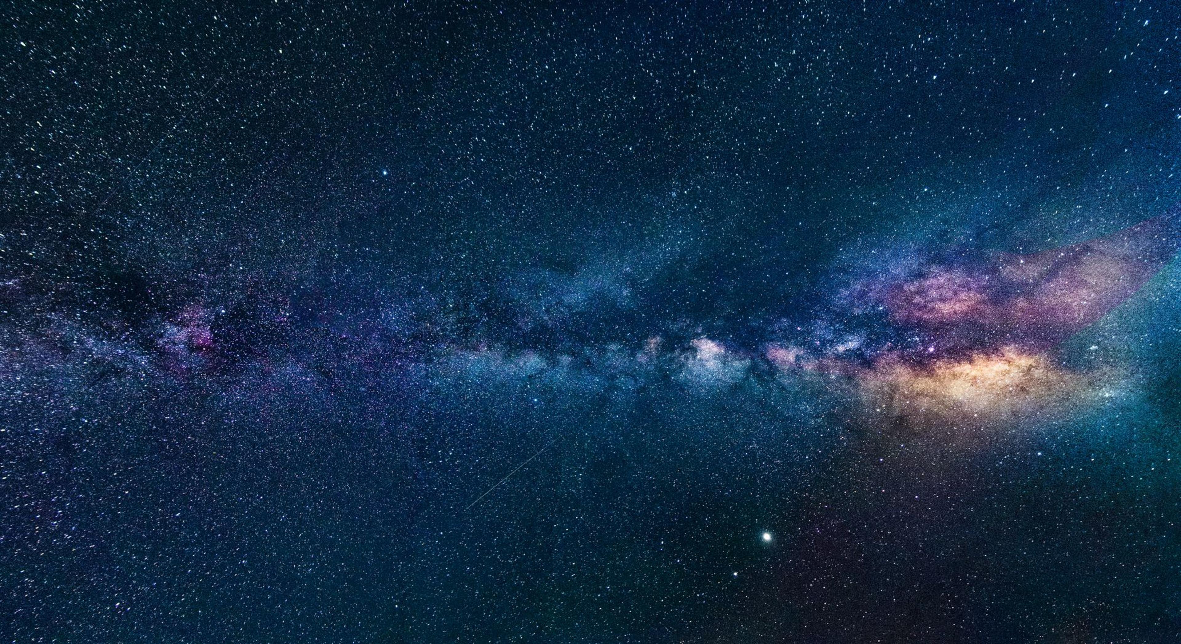 A vast star-filled night sky glowing over a dark silhouetted landscape