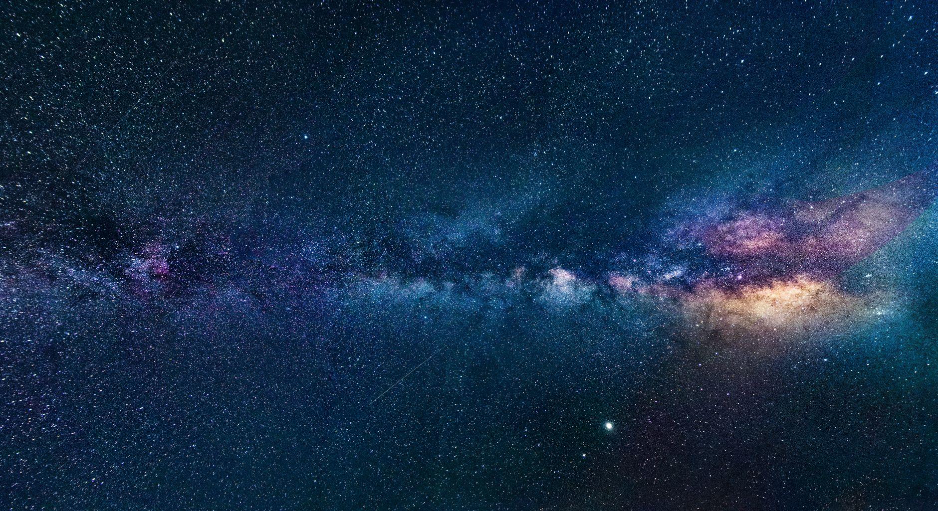 A vast star-filled night sky glowing over a dark silhouetted landscape