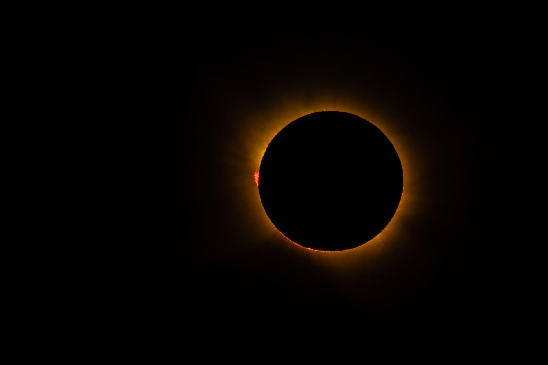A total solar eclipse glowing with a bright corona against a darkened sky