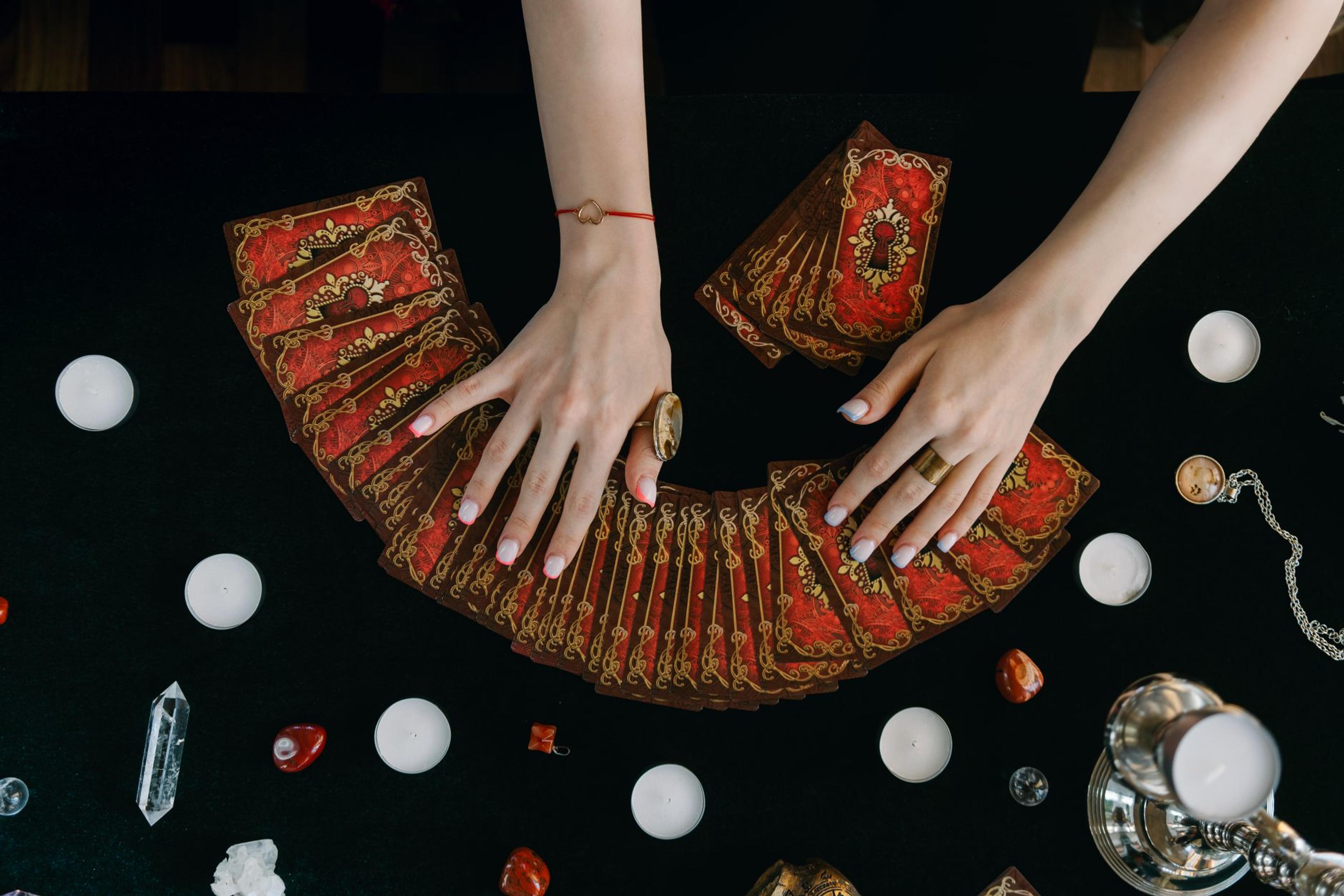 Hands arranging tarot cards on a table surrounded by candles and crystals