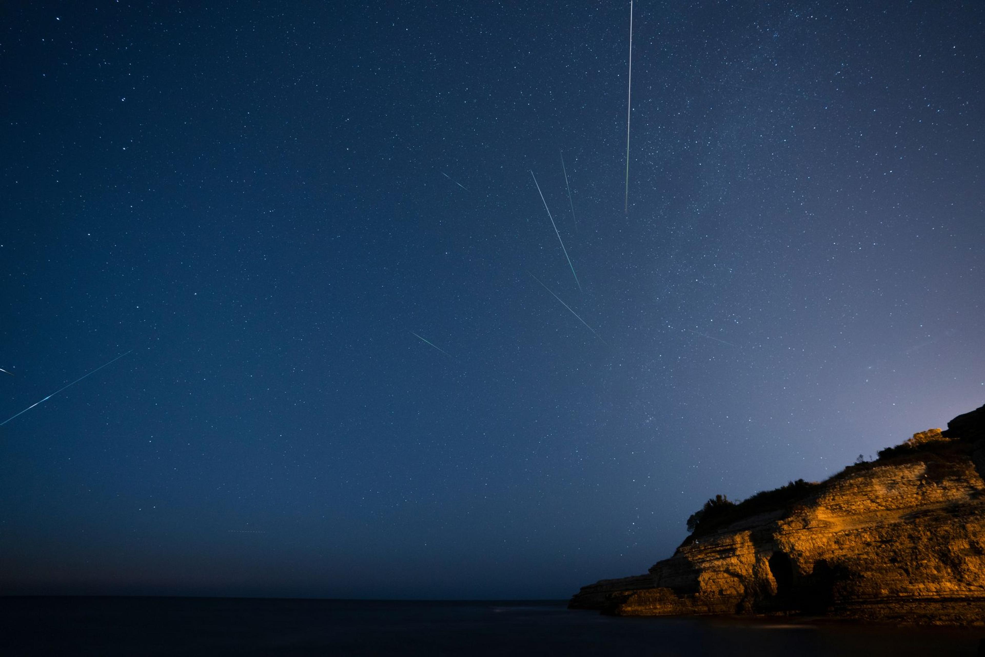 A dark starry night sky with a meteor streaking over a rocky cliff during the Perseid meteor shower