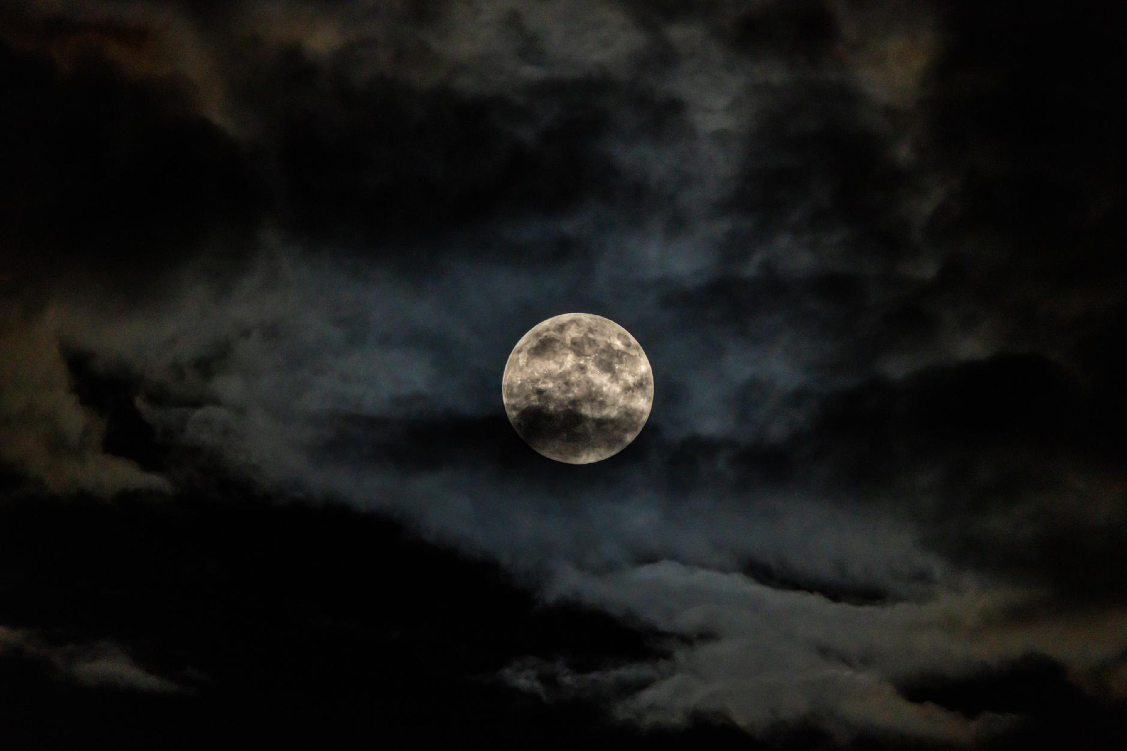 A dramatic full moon glowing behind dark clouds in a night sky