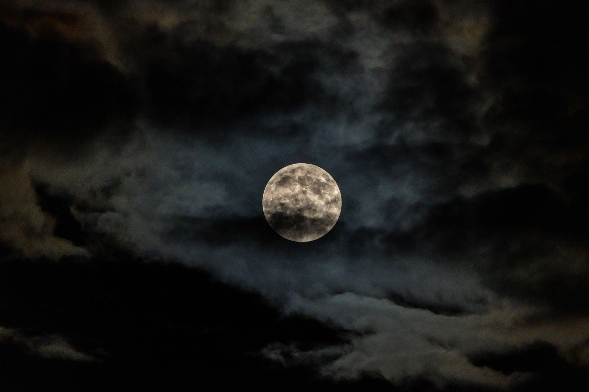 A dramatic full moon glowing behind dark clouds in a night sky
