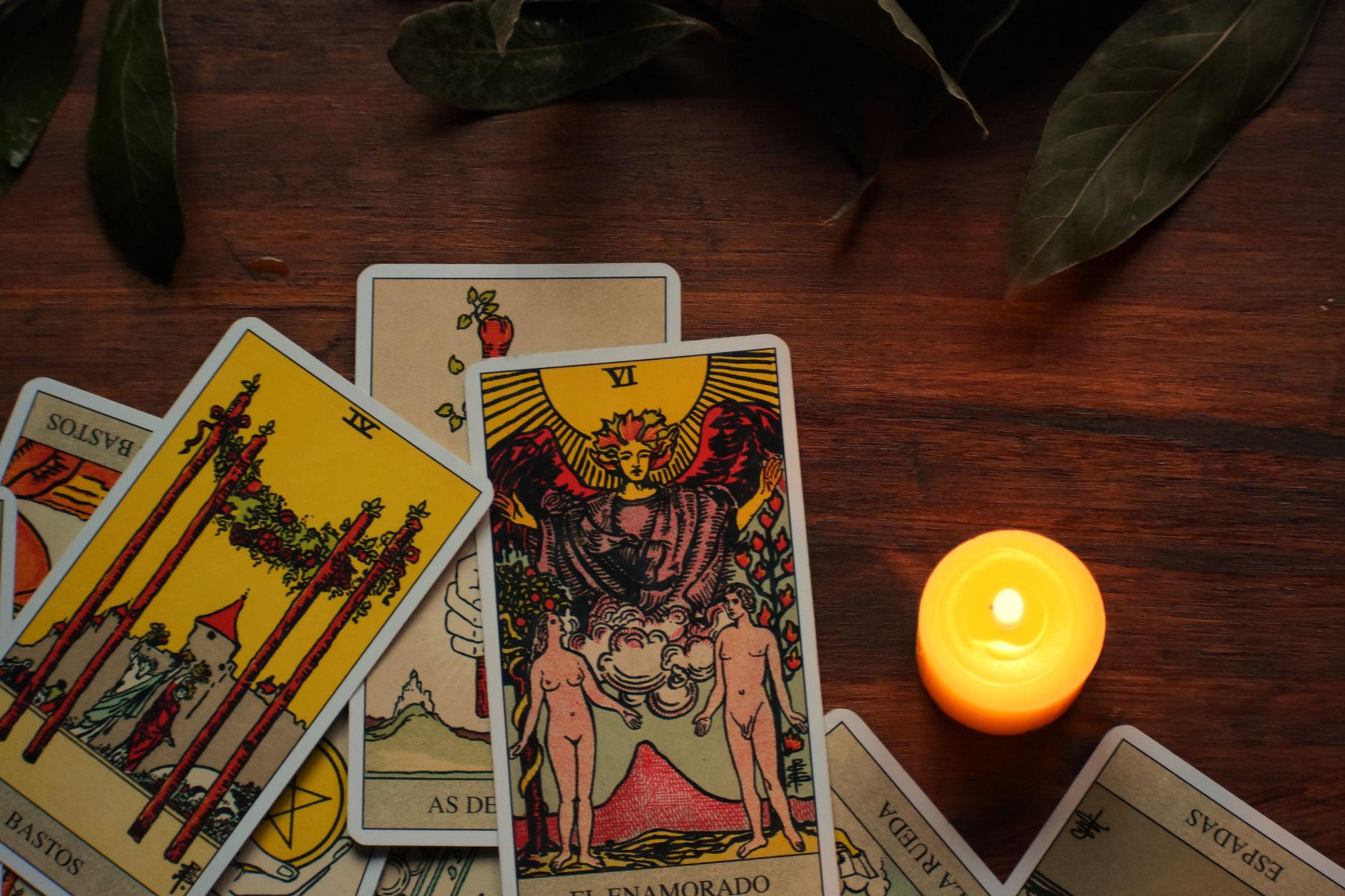 Tarot cards spread on a table beside a lit candle in a dim, mystical room