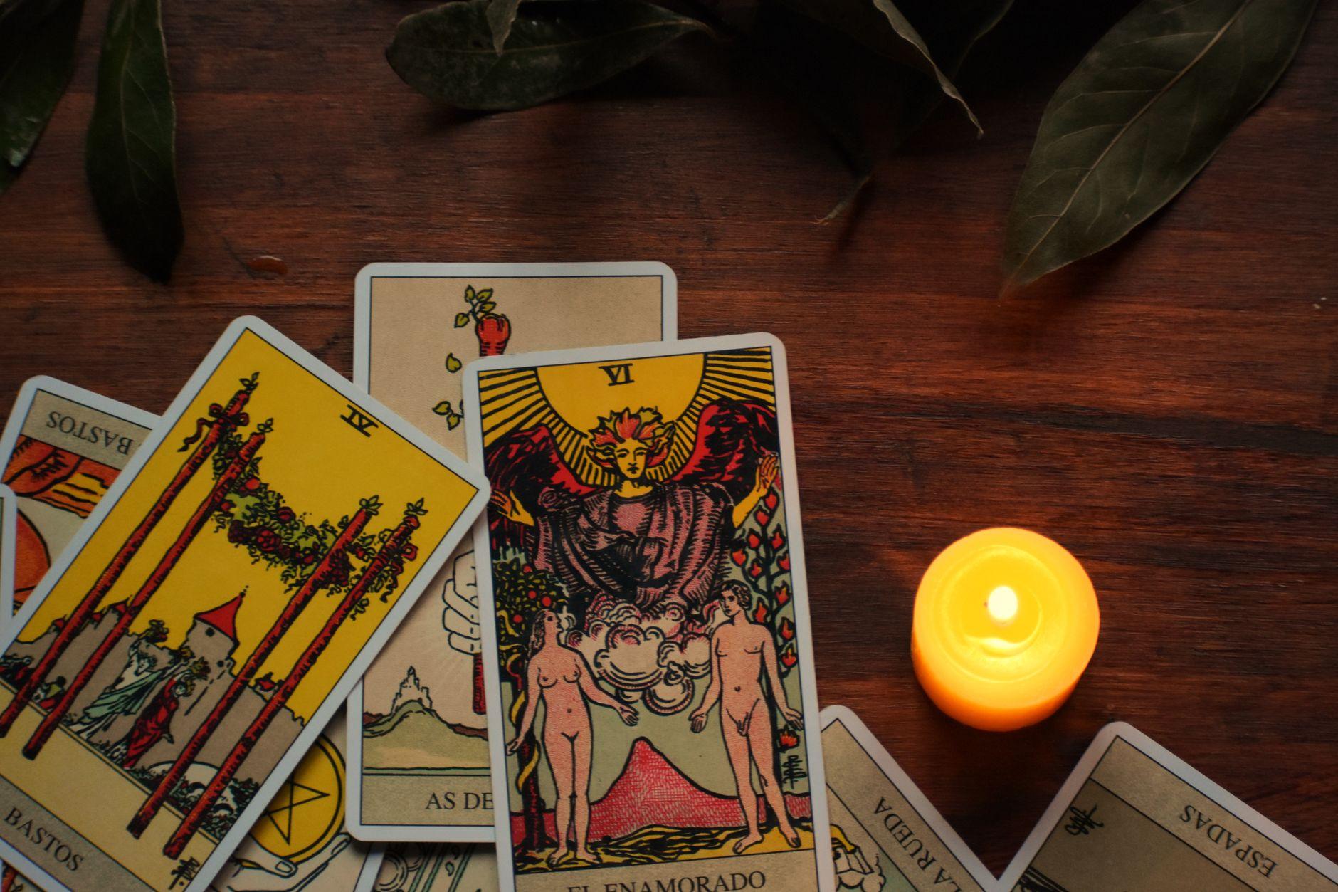 Tarot cards spread on a table beside a lit candle in a dim, mystical room