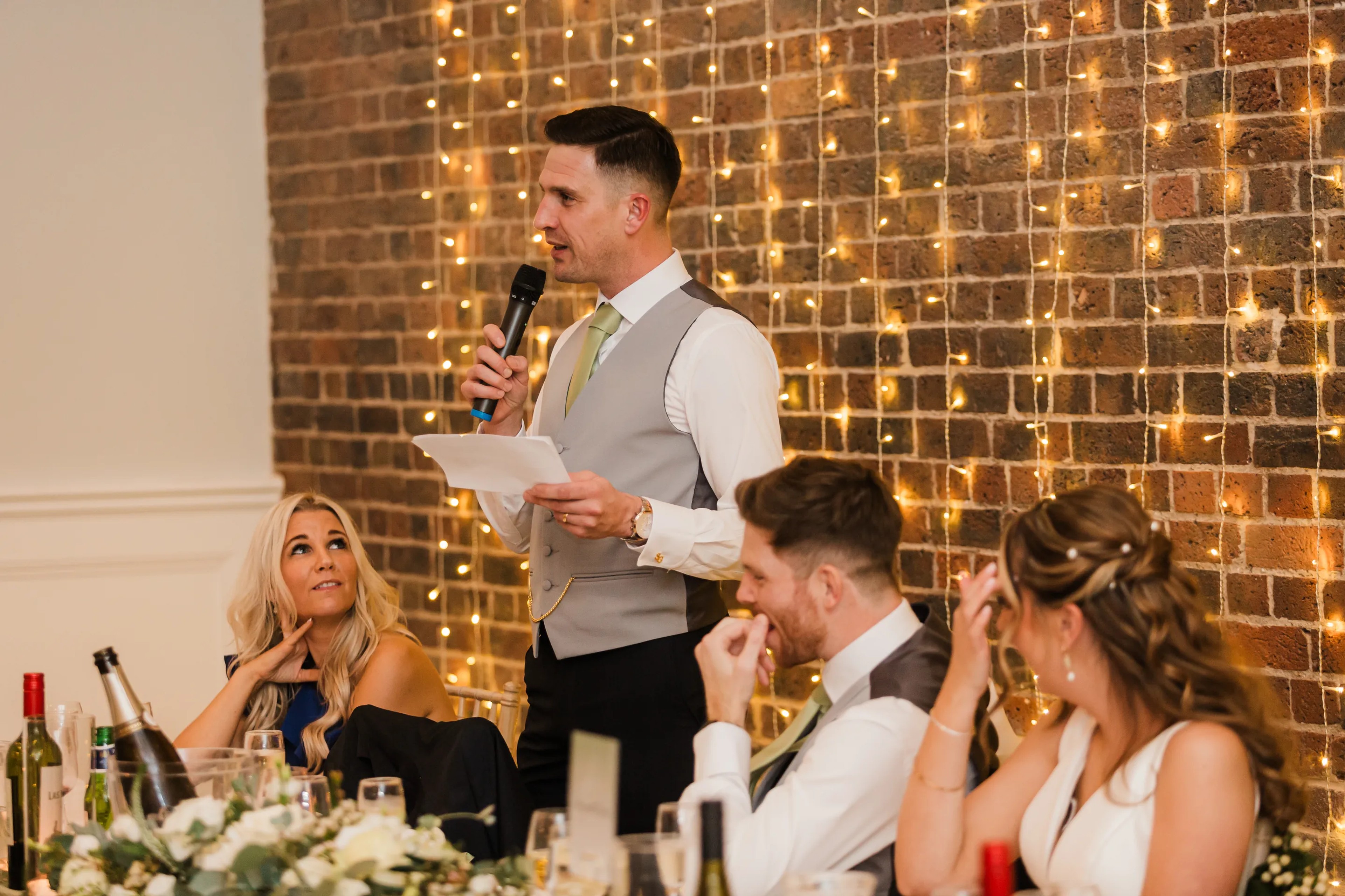 Best man delivering wedding speech with fairy lights