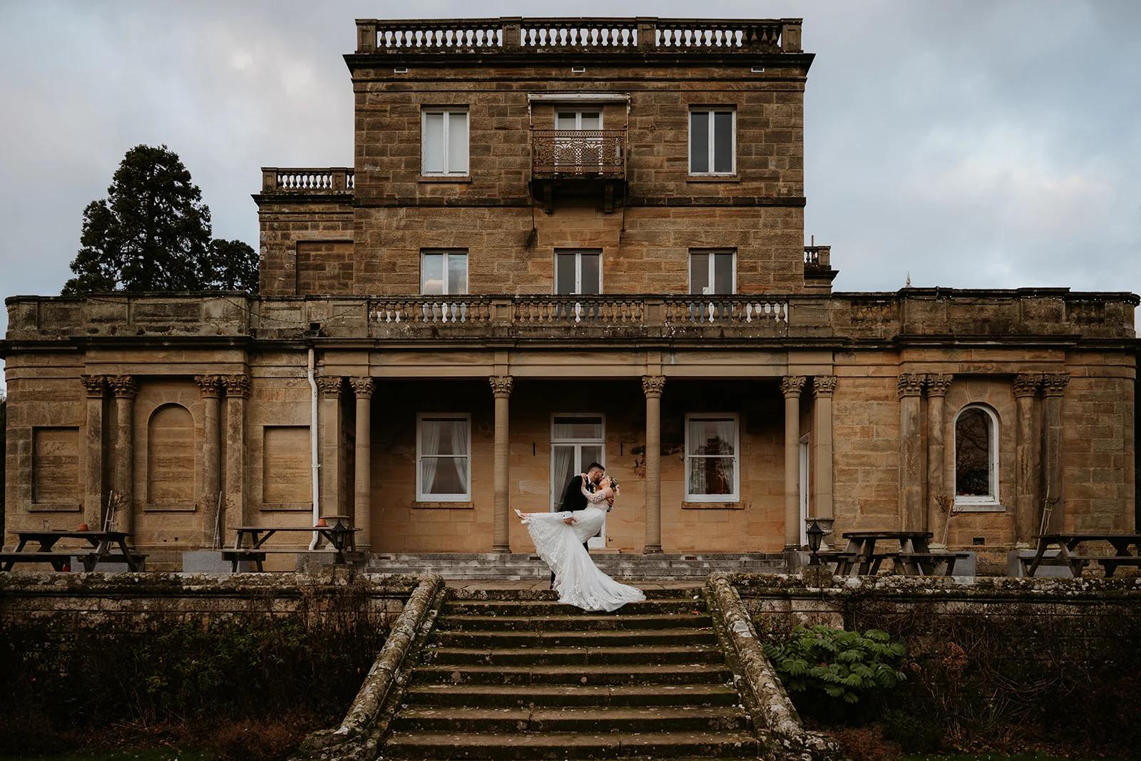 Wedding couple in front of the full manor house facade with dramatic sky