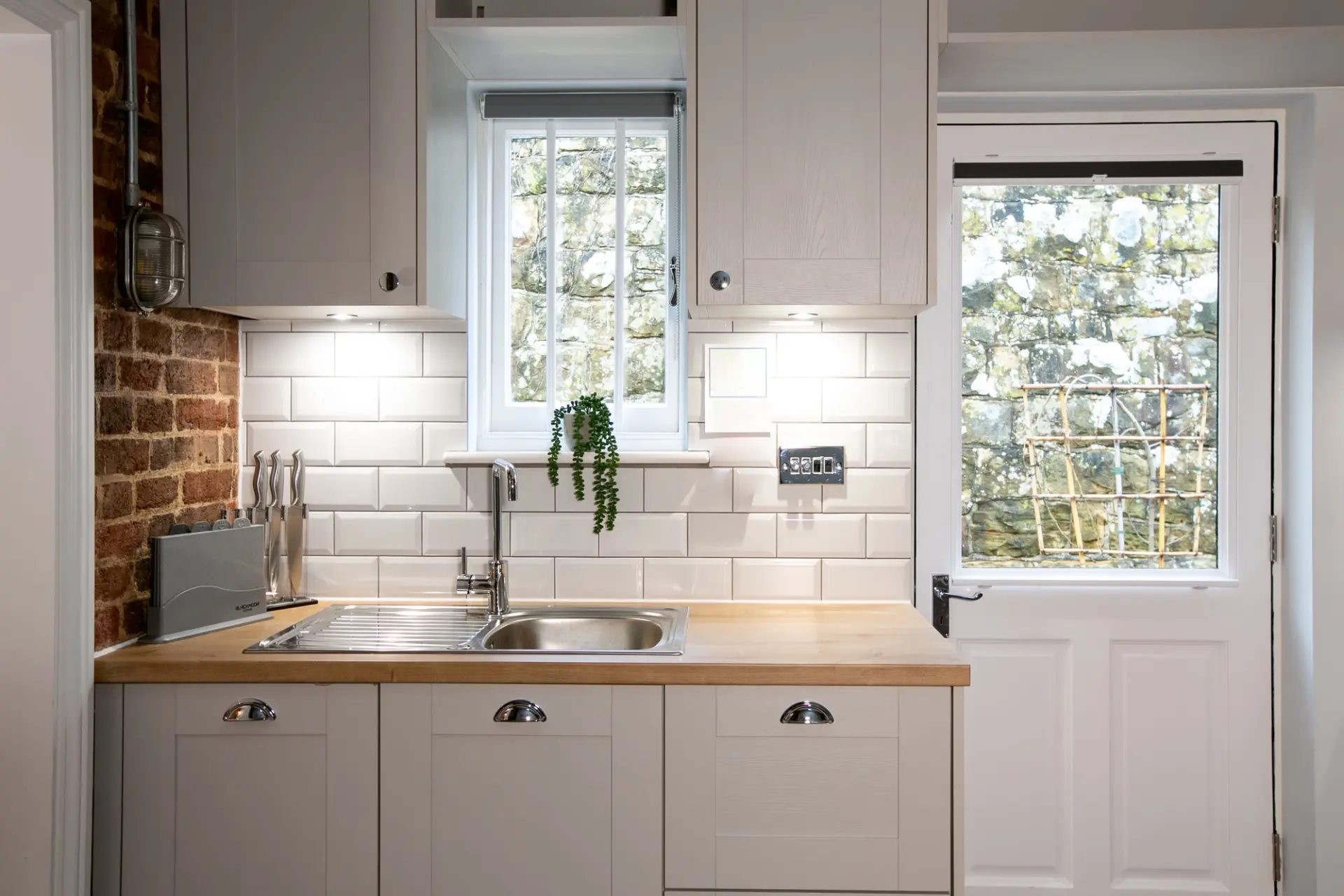 Fully equipped kitchen with metro tiles, exposed brick and a garden door in a Garden Cottage at Salomons Estate