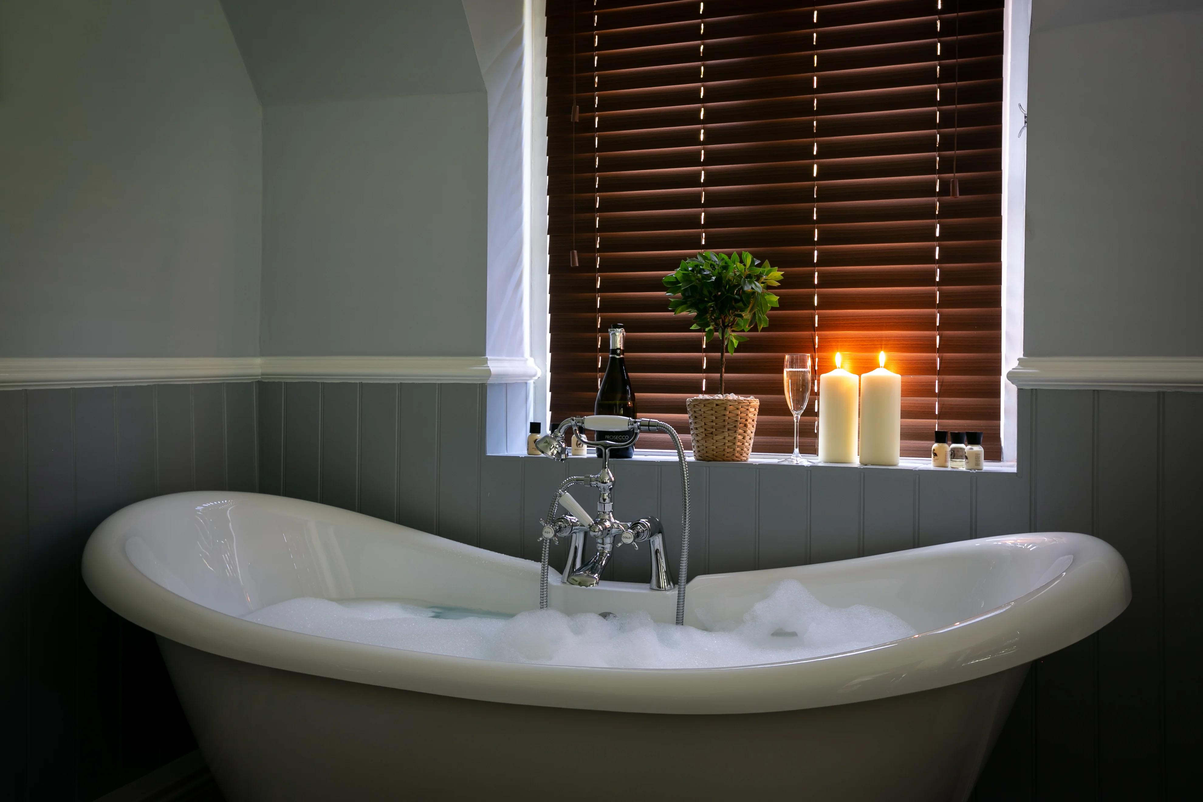 Luxury freestanding bathtub with champagne and candles in cottage bathroom