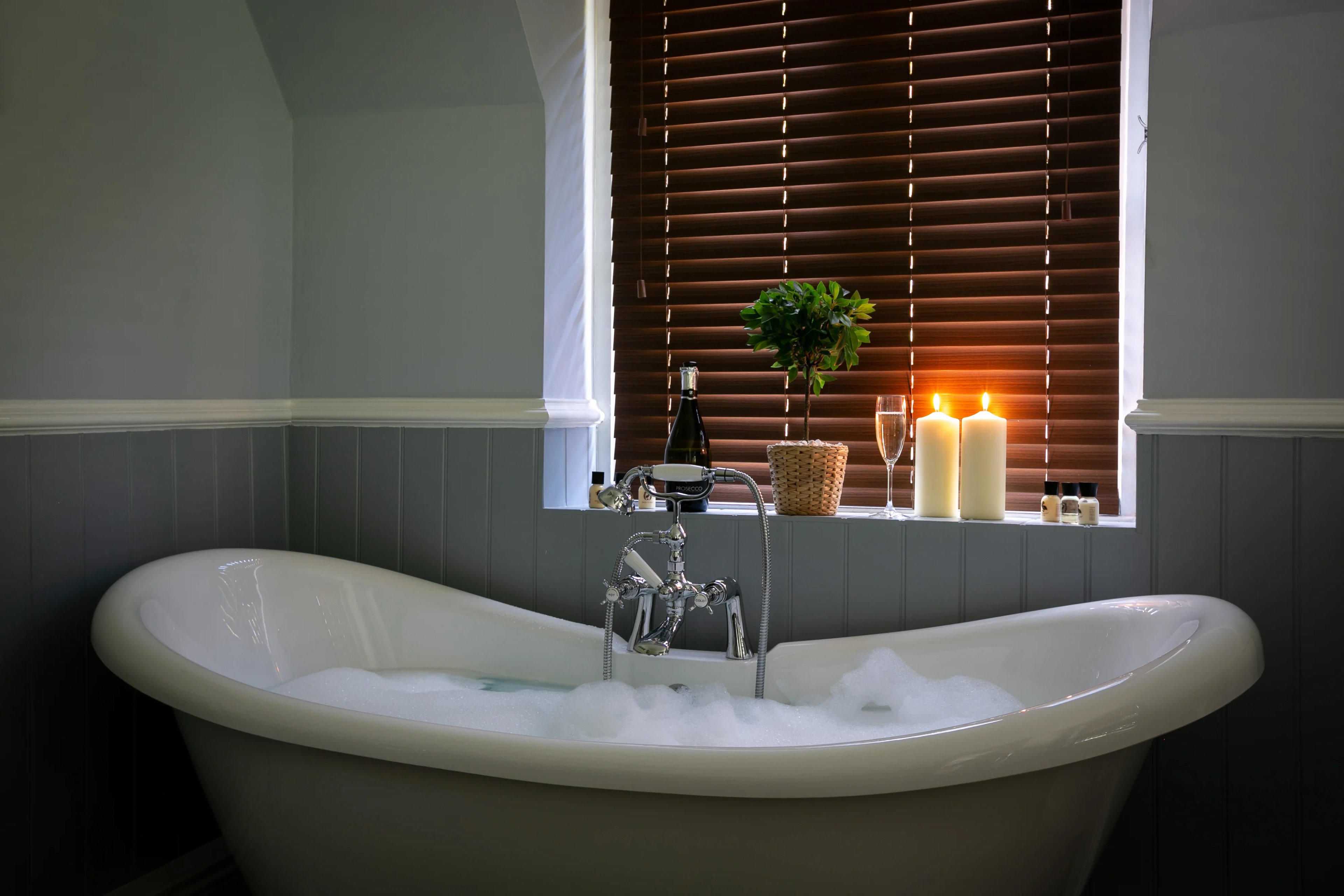 Luxury freestanding bathtub with champagne and candles in cottage bathroom