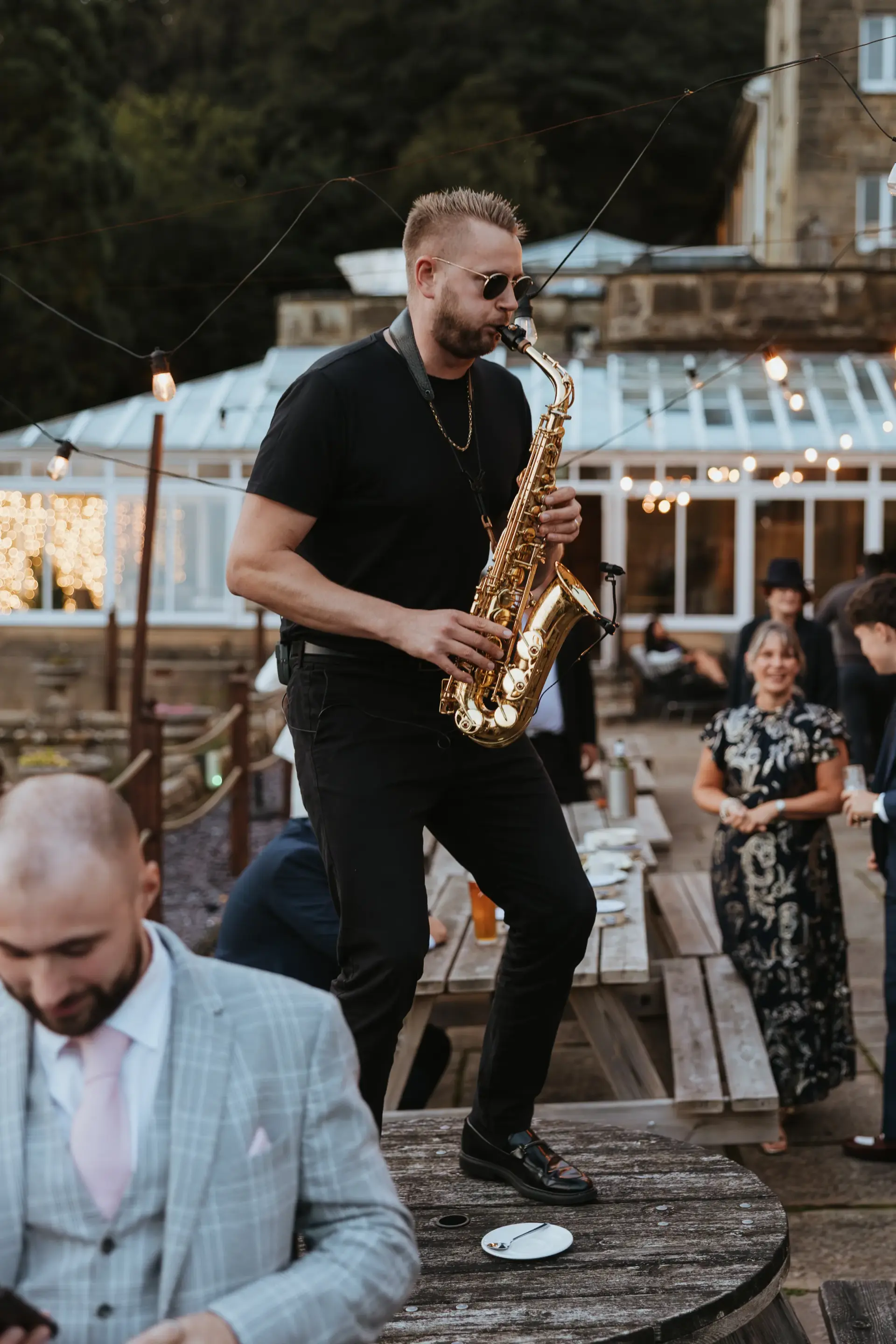 Saxophonist playing on a table among wedding guests at dusk at Salomons Estate