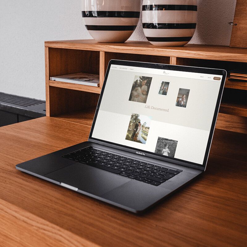 Laptop with modern showit website displayed sitting on wooden desk with pottery.