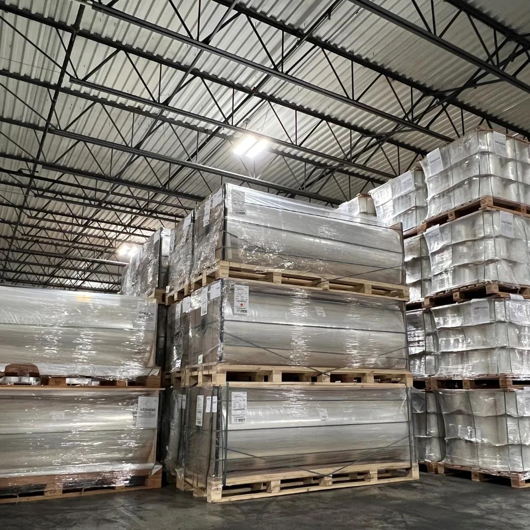 Stacked film rolls in PennPac stocking warehouse Stacked pallets of large plastic-wrapped flexible film rolls inside a high-ceiling warehouse.