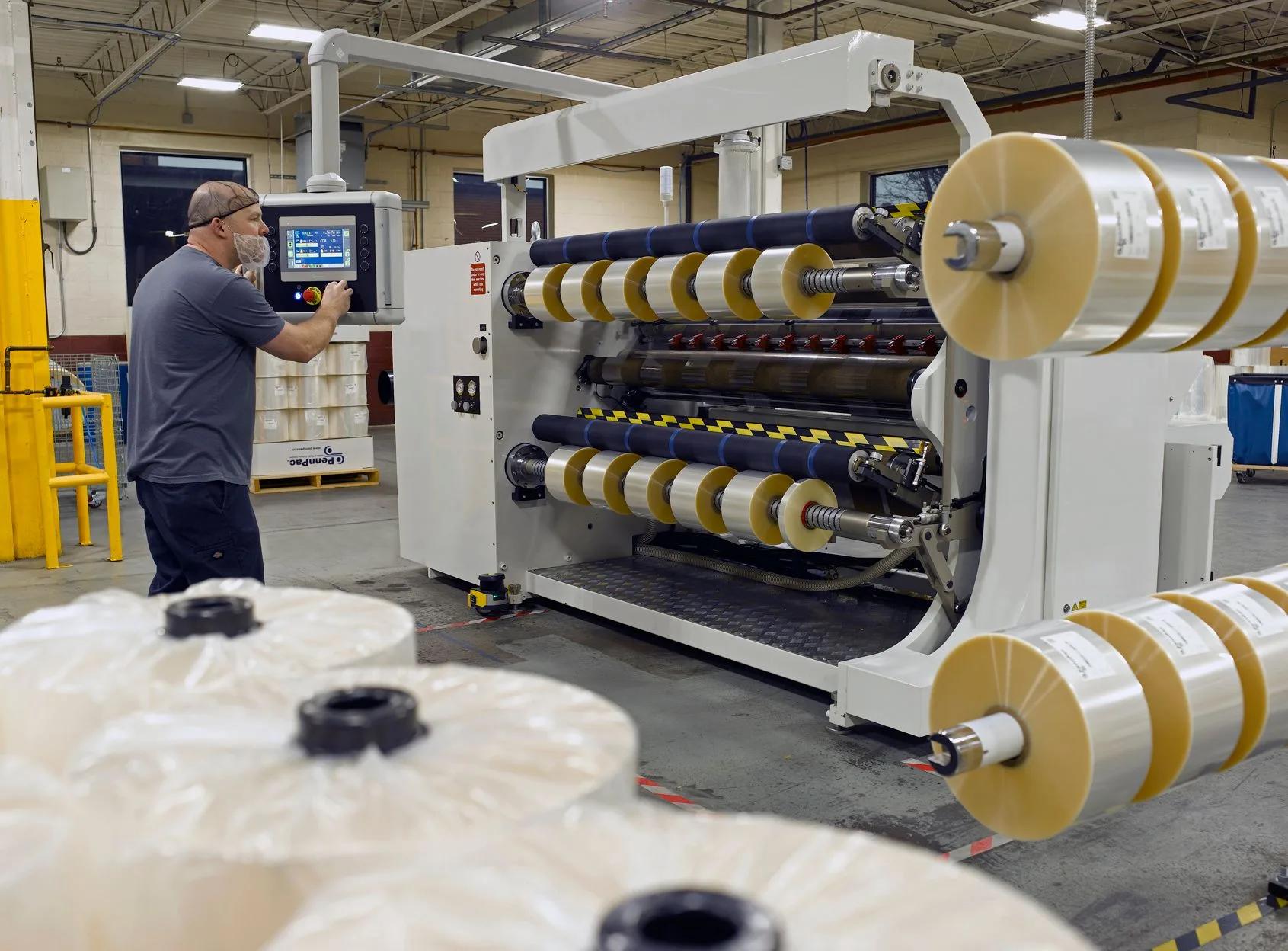 Slitting machine operator Operator at touchscreen beside a slitting machine with yellow-wound slit rolls and large parent film rolls in foreground.
